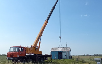 Żuraw koloru żółtego podnoszący budynek w kolorach biało-niebieskich.