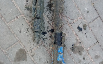 To zdjęcie przedstawia dwa skorodowane, metalowe elementy instalacji z niebieskimi akcentami, leżące obok siebie na chodniku z kostki brukowej.